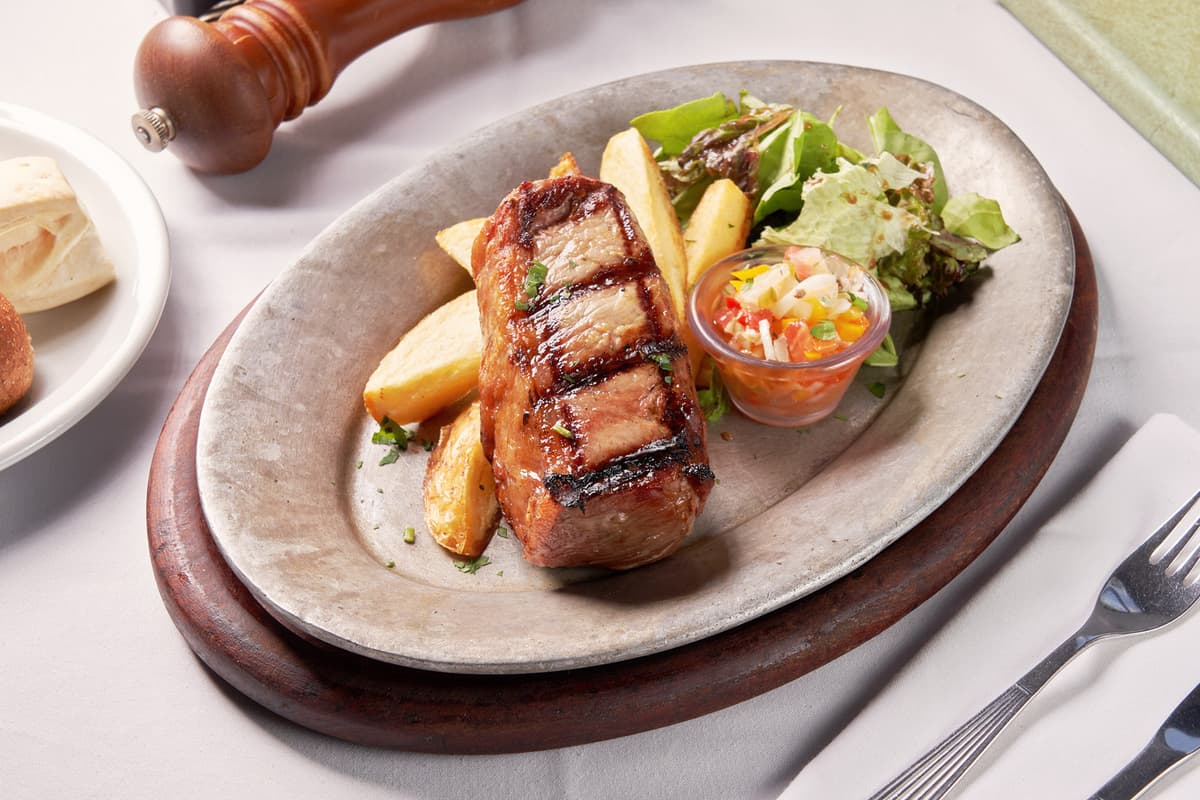 Bife de chorizo sobre colchon de hojas de verdes y papas rusticas